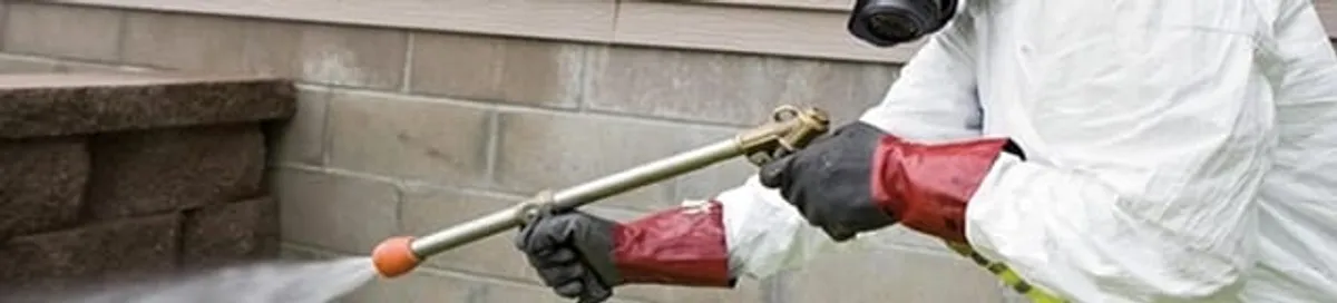 Pest control technician applying exterior insect treatment along a home foundation in Milwaukee, WI