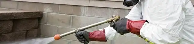 Pest control technician applying exterior insect treatment along a home foundation in Milwaukee, WI