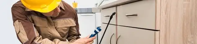Roach exterminator applying treatment under kitchen cabinets in Milwaukee, WI