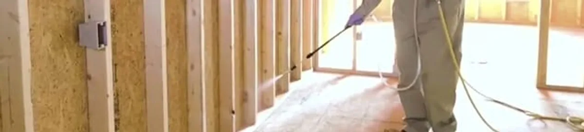 Termite treatment technician applying spray along framing and unfinished walls in Milwaukee, WI